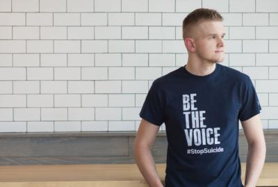 Sam Eaton, founder of Recklessly Alive, wearing a black t-shirt with text: Be the Voice #StopSuicide