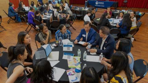 Photo of last year's Asian American Conference attendees sitting at round tables having a discussion and networking