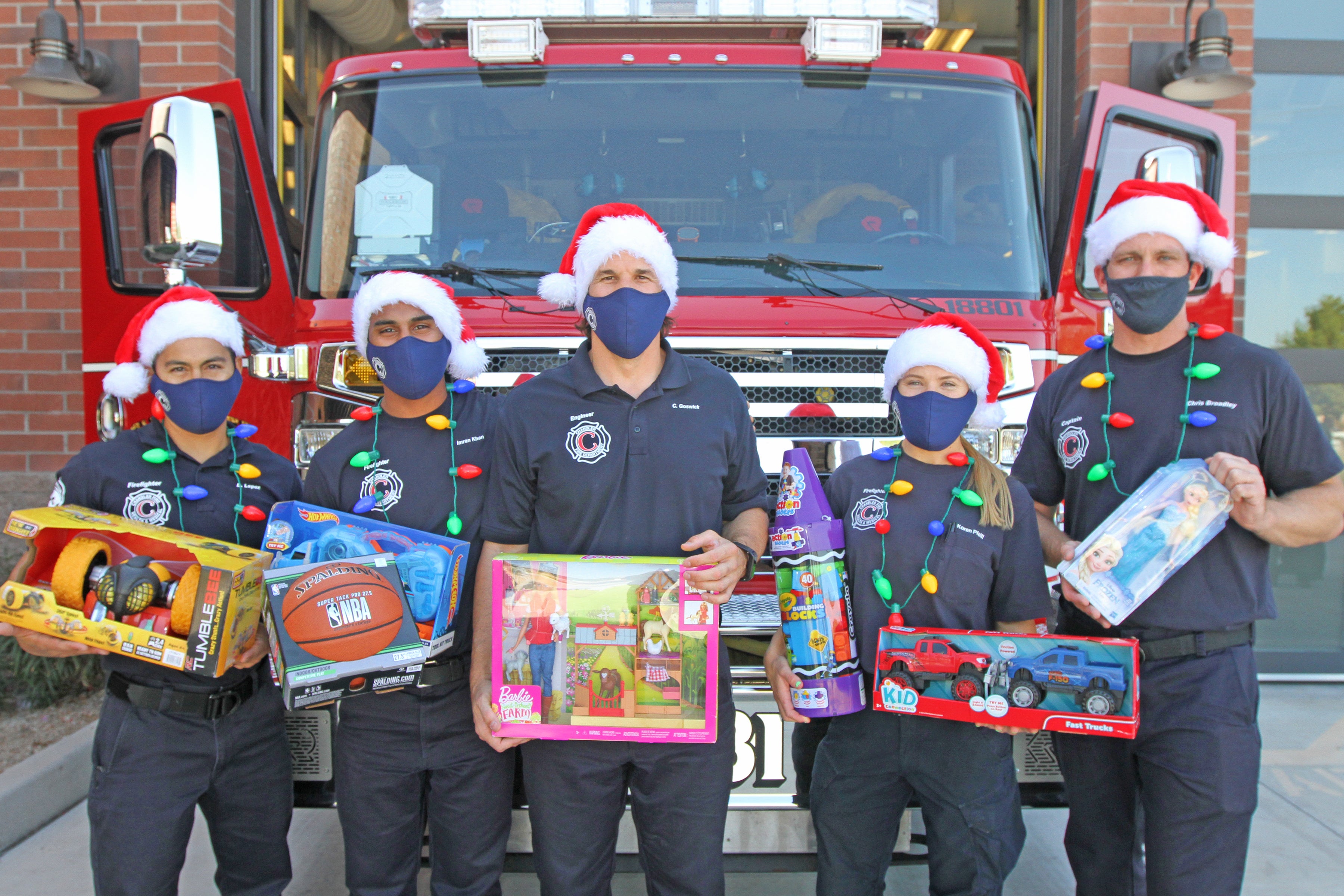 Chandler Firefighters hold toys in front of a firetruck.