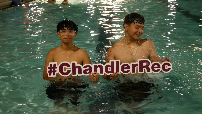 two male teens in the pool at night holding a Chandler Rec sign. 