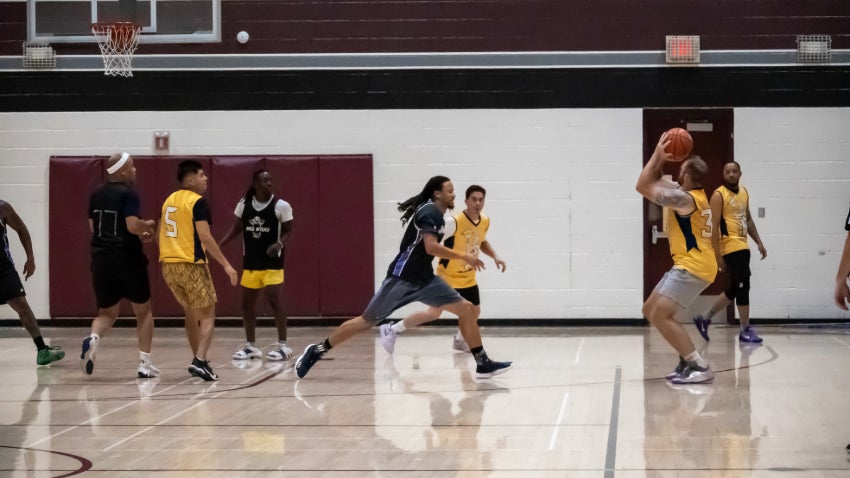 two men's basketball teams, one wearing yellow and one wearing black jerseys. 