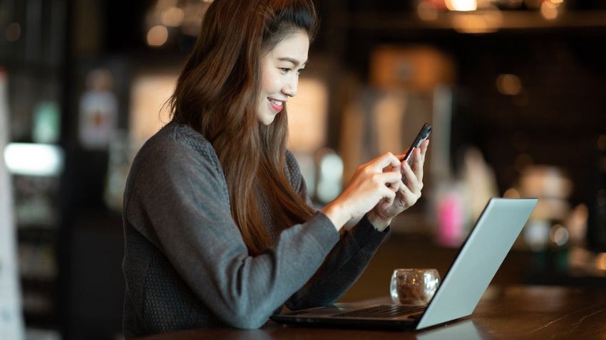 Woman sitting in front of a laptop checking her mobile phone