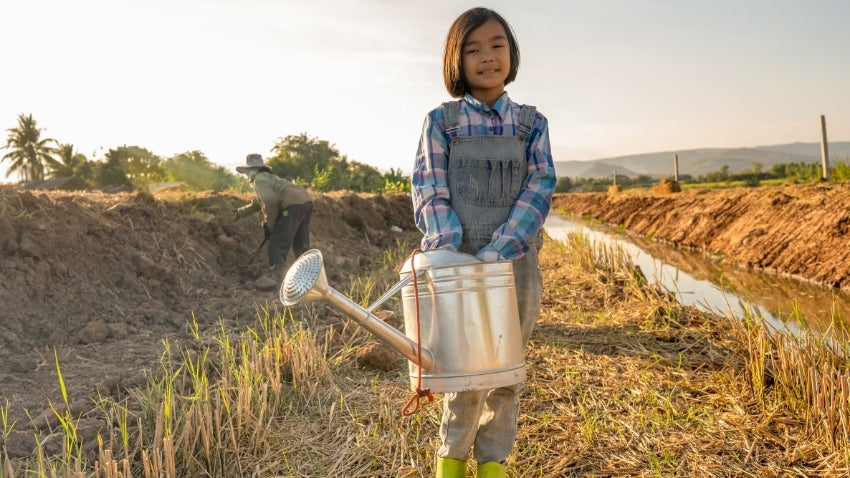 Child uses watering can to water plant in a field
