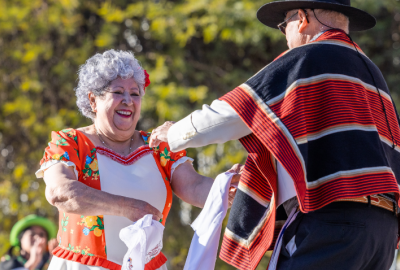 Woman in orange and white dress dancing with man in black and orange poncho