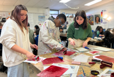 Girl and boy painting red canvases while a woman teaching looks on