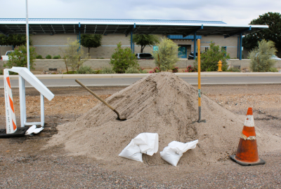 Sandbag station with a huge pile of sand, sandbags and shovels. City facility in the background.