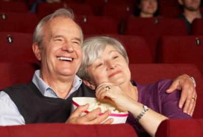 Senior couple enjoying a movie at the theatre while sharing a tub of popcorn