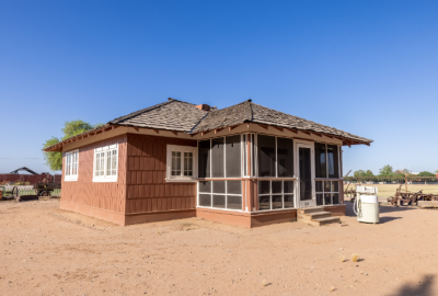 Brown shingled home with a screened-in front porch sits outdoors on a dirt lot at Tumbleweed Ranch in Chandler, Ariz.