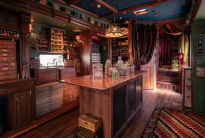 A dark, moody room with dark wood shelves and a bar that are covered in knick-knacks and glass jars
