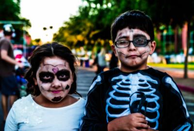 Two kids with spooky face paint and costumes at an outdoor Halloween festival