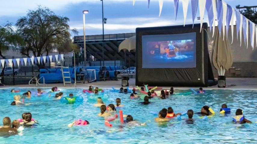people swimming and watching a movie in the pool 