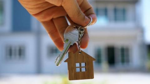 Photo of person holding a key with a "home" keychain