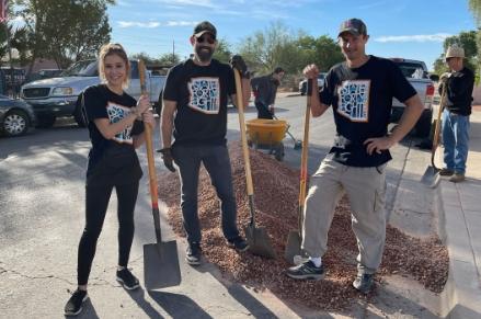 Three volunteers at For Our City Day with shovels and large pile of rock