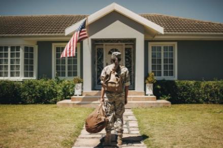 Female veteran in uniform holding a bag facing a house