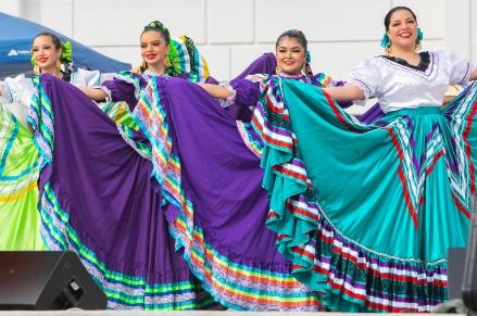 Four female ballet folkorico dancers standing next to each other while holding their colorful skirts