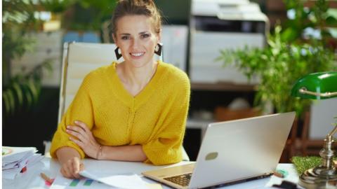 Woman in a yellow blouse sitting at a desk with a laptop