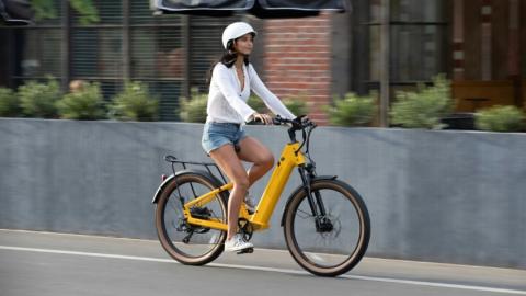 Woman wearing a white helmet riding yellow E-bike along concrete path.