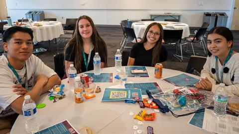 Four young adults sit around a table smiling at the camera