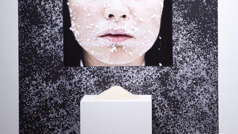 Picture of a woman's nose and mouth in front of a pedestal with clay rice