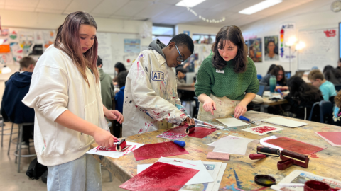 Girl and boy painting red canvases while a woman teaching looks on