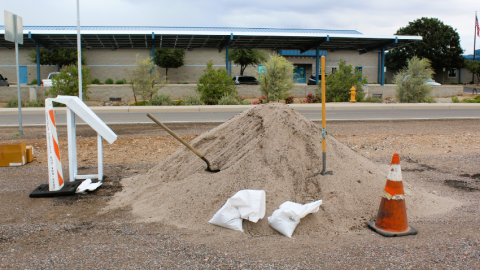 Sandbag station with a huge pile of sand, sandbags and shovels. City facility in the background.
