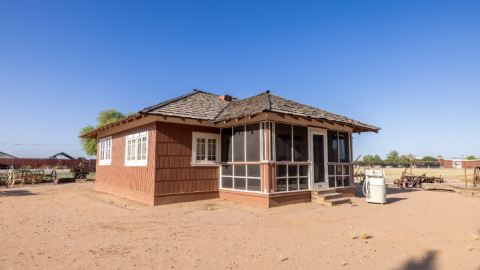 Brown shingled home with a screened-in front porch sits outdoors on a dirt lot at Tumbleweed Ranch in Chandler, Ariz.
