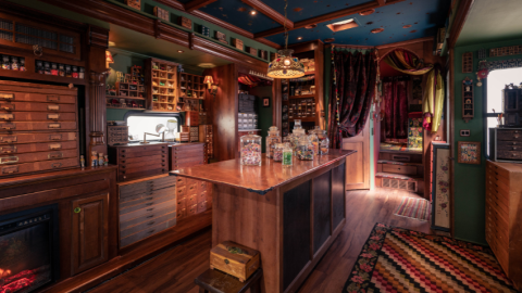 A dark, moody room with dark wood shelves and a bar that are covered in knick-knacks and glass jars
