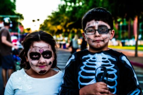 Two kids with spooky face paint and costumes at an outdoor Halloween festival
