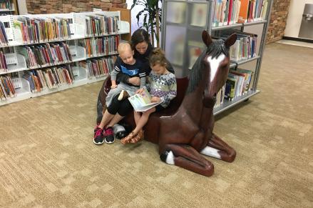 A family reads together on a horse bench at Basha Library.