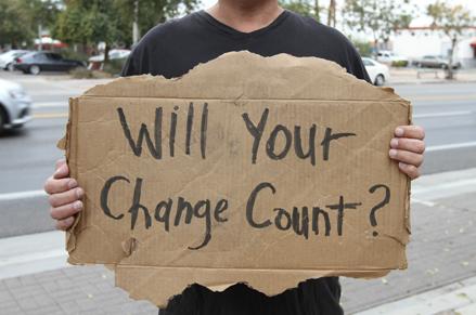 Man holding a sign that says, Will Your Change Count?